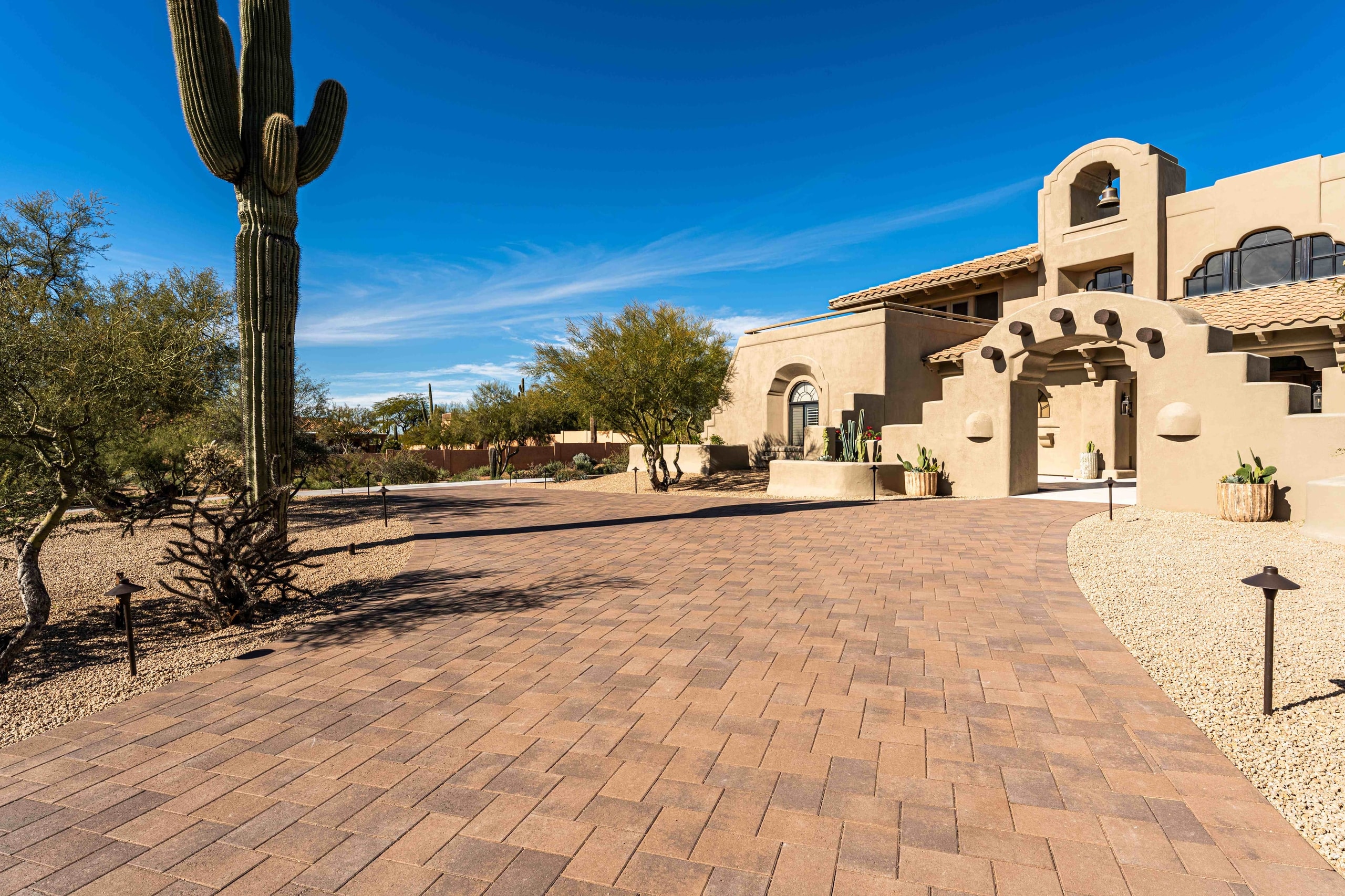 Curved brown paver driveway beside a saguaro leading to a Santa Fe style home in Scottsdale